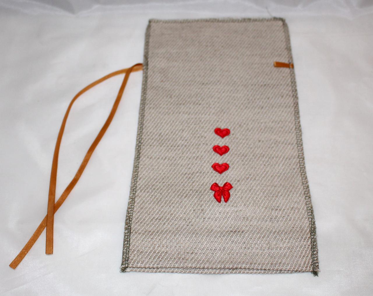 Lniany pokrowiec z haftowanymi czerwonymi sercami i wstążką, idealny na prezent. Minimalistyczny design z subtelnymi detalami.