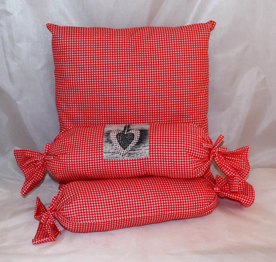 Dekoracyjne poduszki w czerwoną kratkę: prostokątna i dwie w kształcie cukierków z kokardkami. Jedna z sercem na łatce. Idealne jako element wystroju wnętrza.
