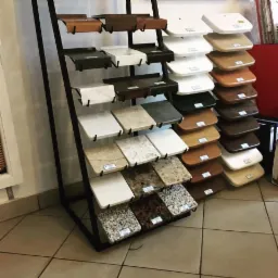 Ekspozycja próbek materiałów wykończeniowych na metalowym stojaku w sklepie, widoczne różne kolory i faktury blatów oraz oklein.