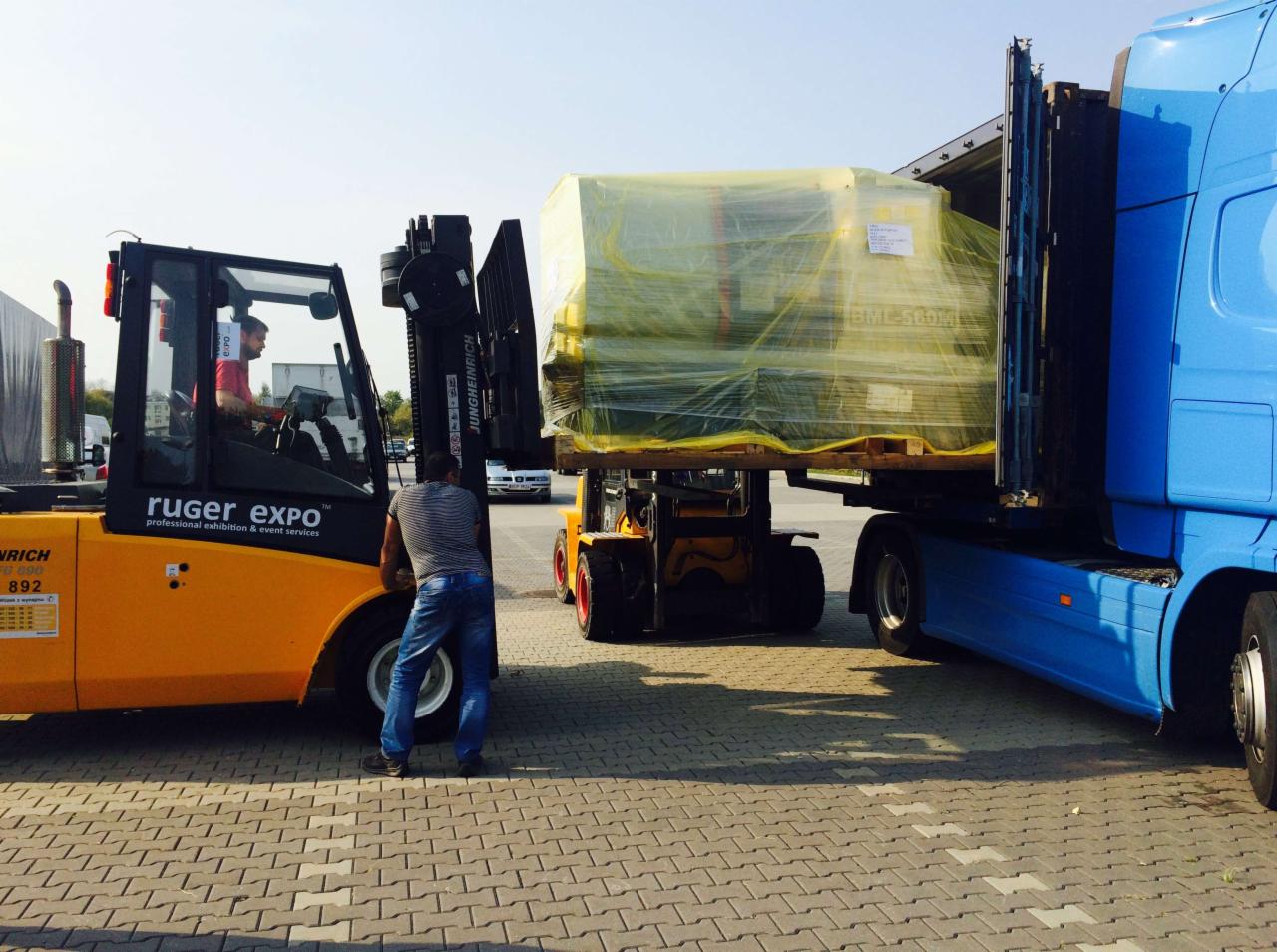 Załadunek maszyny owiniętej folią na ciężarówkę za pomocą wózka widłowego Jungheinrich. Pracownik nadzoruje proces. Ruger Expo w tle.