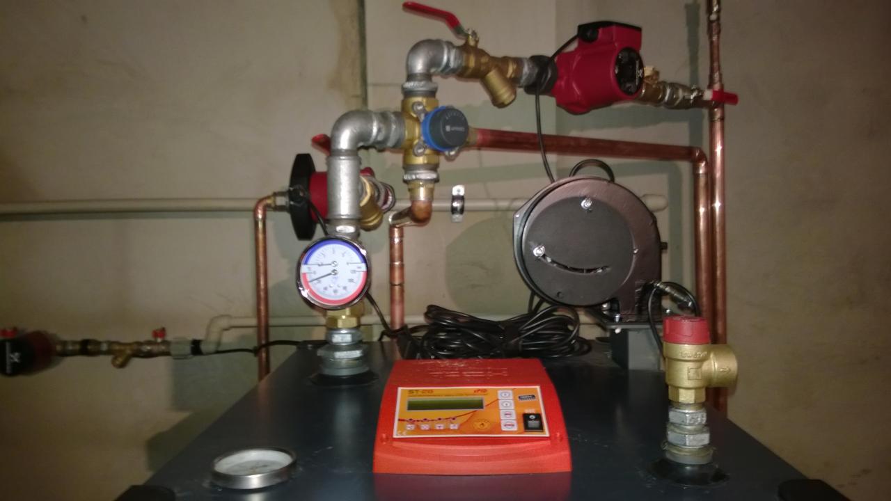 Szczegółowe ujęcie kotłowni z widocznymi rurami miedzianymi, zaworami, pompami obiegowymi, manometrem i sterownikiem ST-28 na kotle, ukazujące skomplikowaną instalację grzewczą.