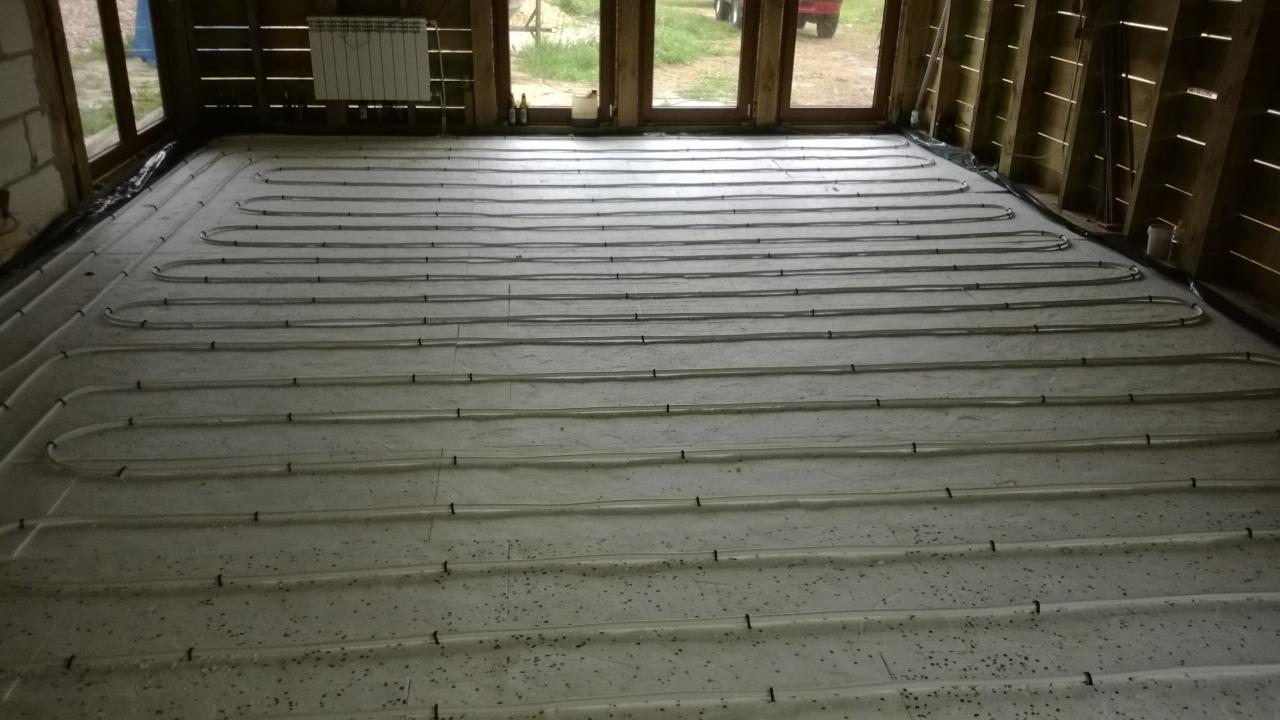 Rozłożona instalacja ogrzewania podłogowego na izolacji w surowym pomieszczeniu z drewnianą konstrukcją ścian.