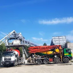 Widok na teren z silosami w kolorach zieleni i żółci, betonomieszarkami MAN oraz pompą do betonu CIFA MAGNUM MK 28, uzupełniony ładowarką kołową HSW.