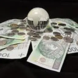 Stos banknotów 100 zł z rozrzuconymi monetami i szklaną kulą z mapą świata na wierzchu, na czarnym tle.