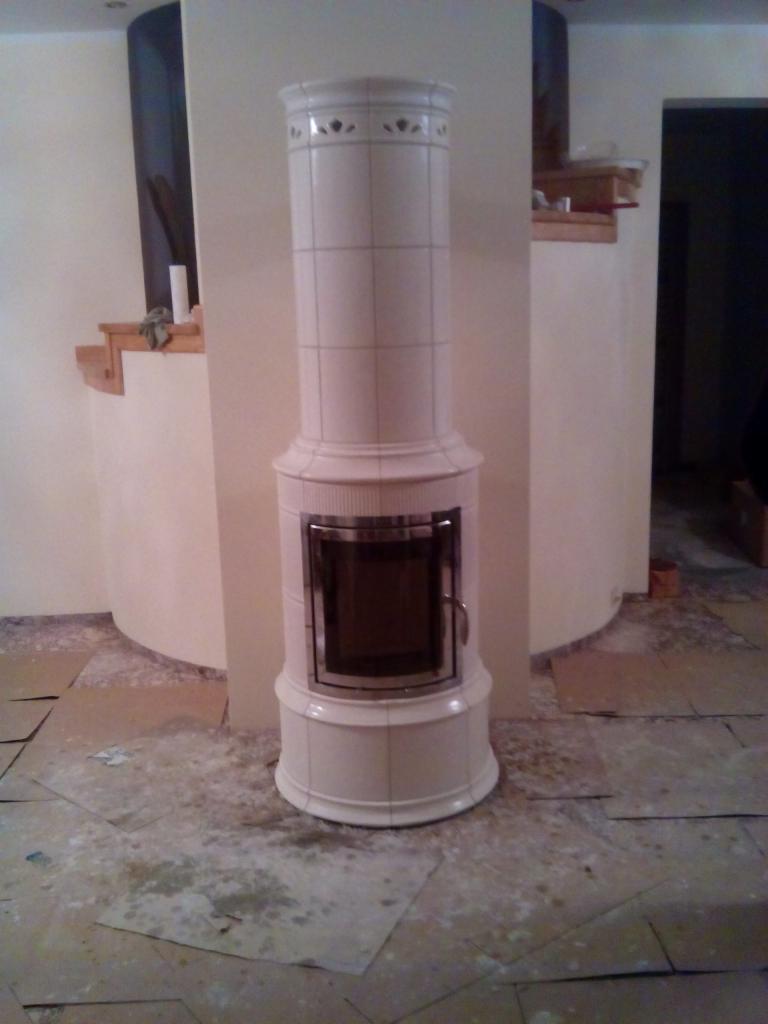 Biały, kaflowy piec kominkowy w trakcie montażu, zabezpieczona podłoga, widoczne niedoskonałości wykończenia.