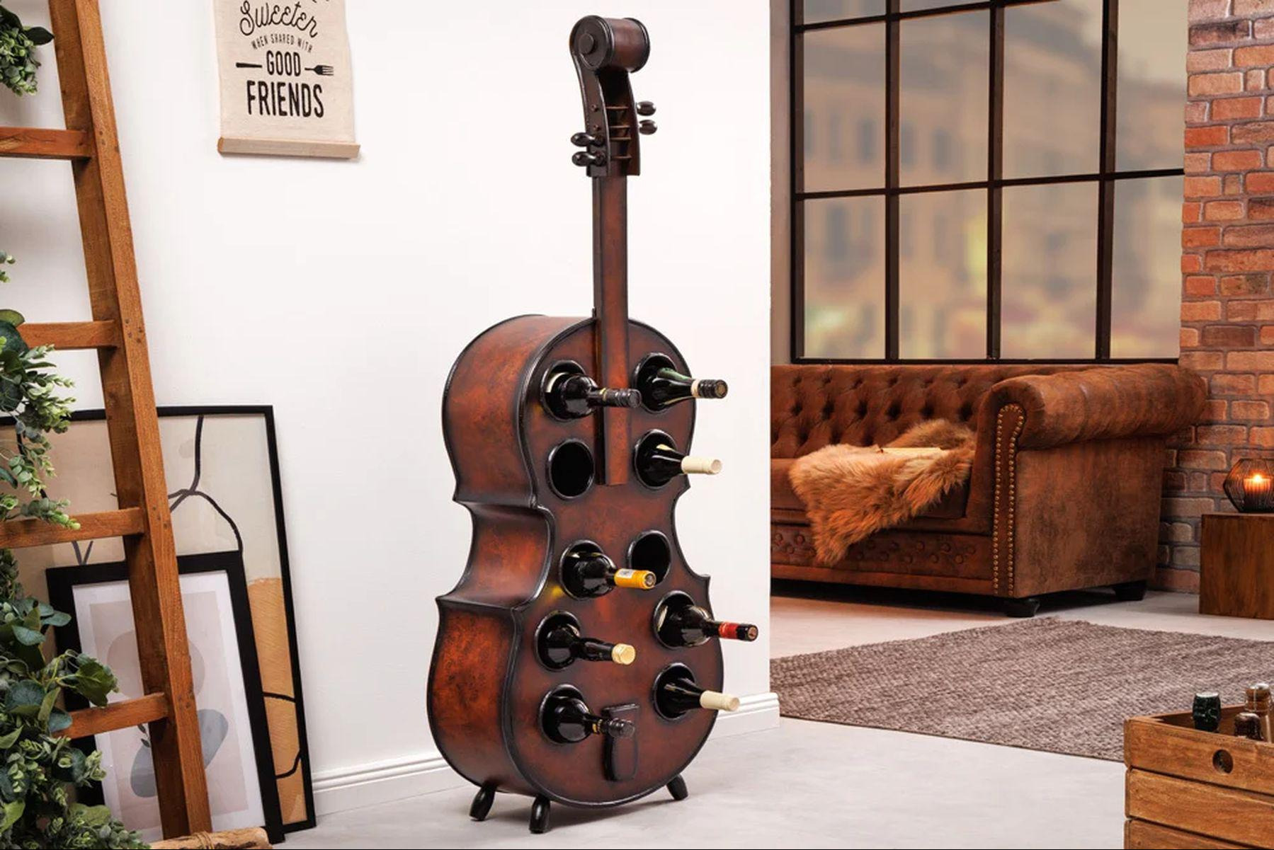 Stojak na wino w kształcie wiolonczeli, wypełniony butelkami, w tle skórzana sofa i ceglana ściana.