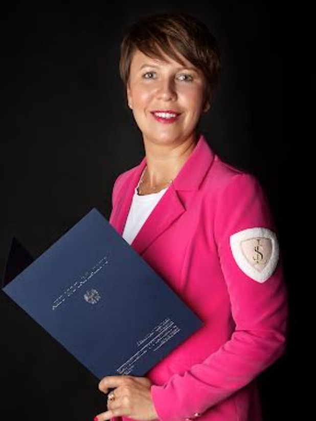 Portret kobiety w różowym żakiecie trzymającej ciemnoniebieską teczkę z dokumentami na czarnym tle.