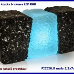 Świecąca kostka brukowa LED RGB 'Piccolo' o wymiarach 5,3x7x9x6cm, otoczona dwoma ciemnymi kostkami. Prezentacja produktu z logo 'Led Qube'.