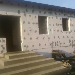 Budowa domu z betonu komórkowego: ściany wzniesione, widoczne otwory okienne i drzwiowe, schody wejściowe. Etap surowy, niezadaszony.