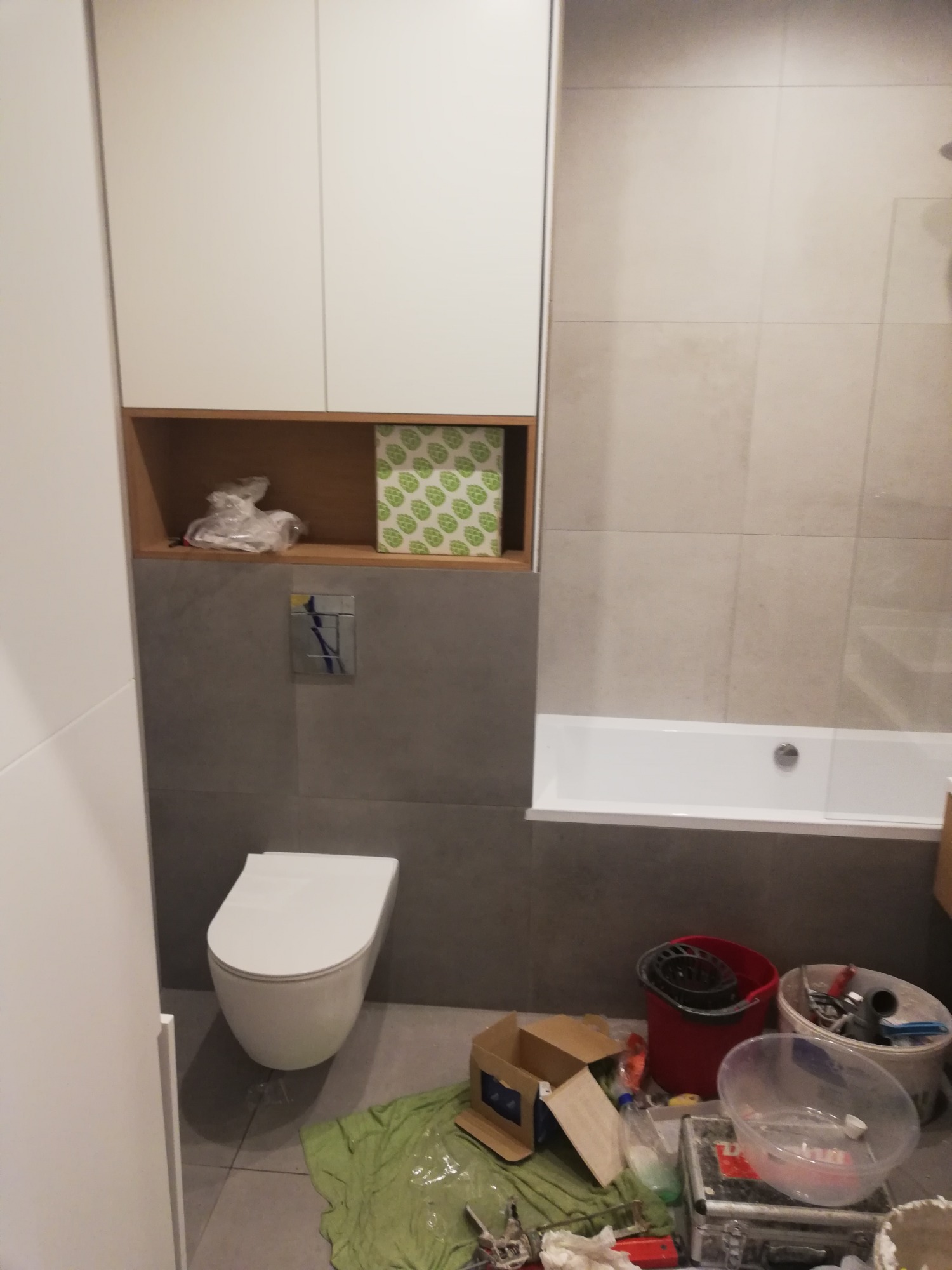 Łazienka w trakcie prac wykończeniowych; widoczna zabudowa meblowa, podwieszana toaleta, wanna oraz liczne narzędzia i materiały budowlane na podłodze.