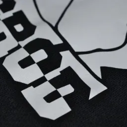 Czarny materiał z białym nadrukiem logo i szachownicą. Detal nadruku wykonanego na tkaninie z bliska, z widoczną strukturą materiału.