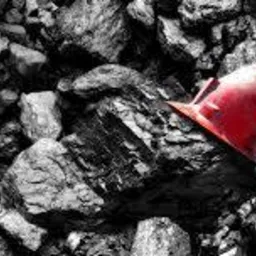 Kupa czarnego węgla kamiennego z czerwonym kaskiem górniczym na wierzchu, oświetlona z góry.