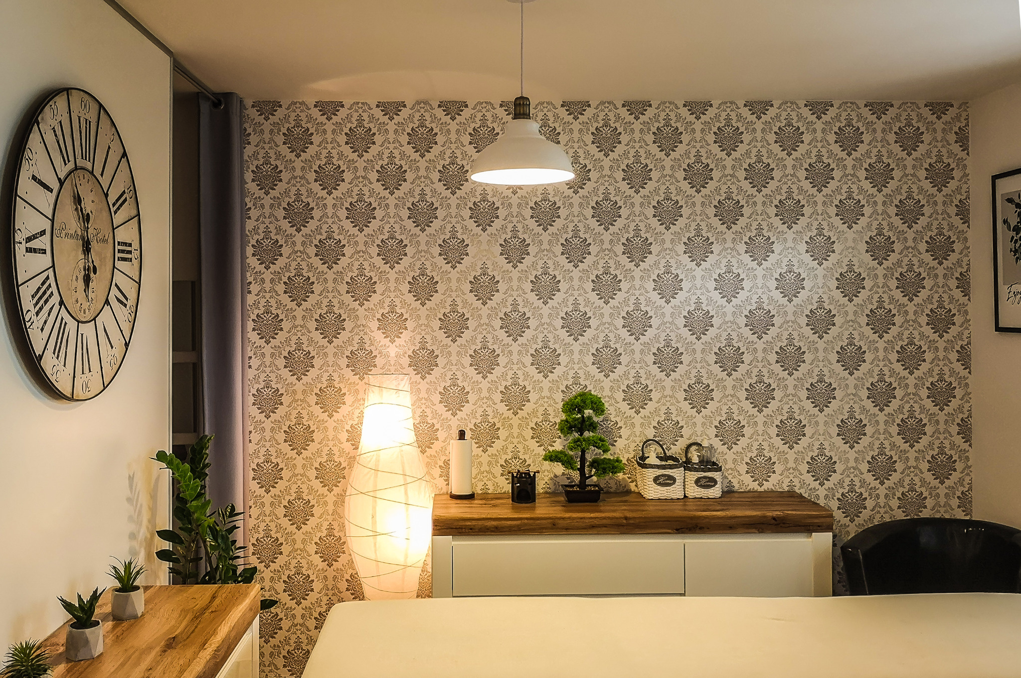 Jasne wnętrze gabinetu z dekoracyjną tapetą, lampą podłogową, bonsai i dużym zegarem na ścianie, tworzące relaksującą atmosferę.