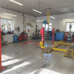 AutoPunkt 24 - Wnętrze warsztatu samochodowego z dwoma podnośnikami kolumnowymi w kolorze czerwonym i żółtym, narzędziami i wyposażeniem warsztatowym pod ścianami, oraz oświetleniem jarzeniowym.