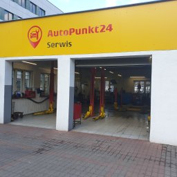 AutoPunkt 24 - Widok z zewnątrz na warsztat samochodowy AutoPunkt24 z trzema stanowiskami, każdy wyposażony w podnośnik kolumnowy, widoczne narzędzia i wyposażenie wewnątrz.