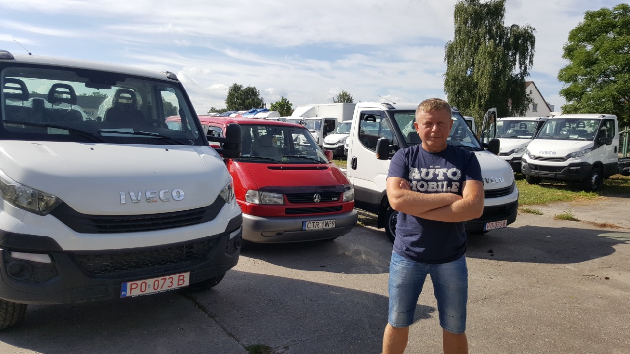 Mężczyzna stoi na tle zaparkowanych busów Iveco i Volkswagena Transportera, widoczny numer rejestracyjny PO-073B na jednym z pojazdów.