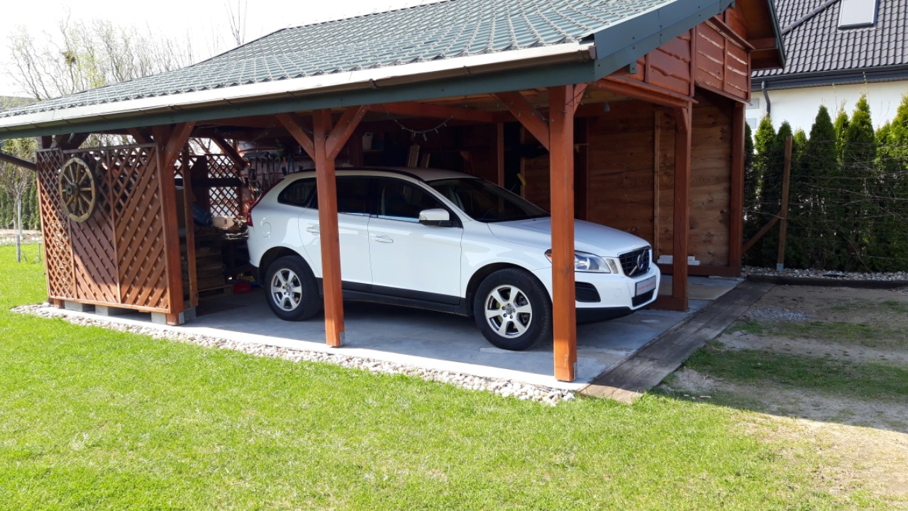 Biały samochód osobowy marki Volvo zaparkowany w drewnianej wiacie z dekoracyjnym kołem od wozu na bocznej ścianie.