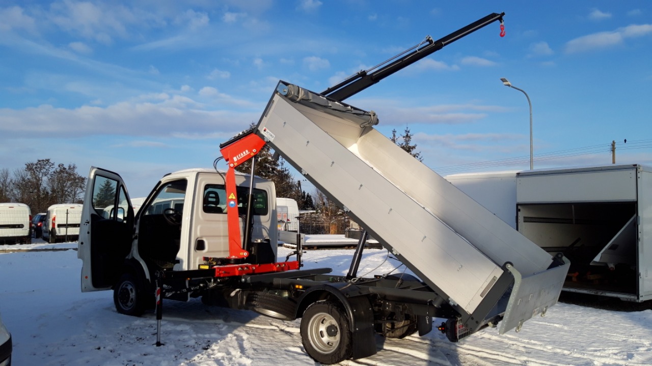 Biały samochód dostawczy z otwartymi drzwiami i podniesioną skrzynią ładunkową z zamontowanym dźwigiem na tle zimowego krajobrazu.