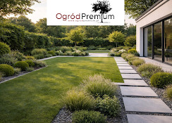 Zadbany ogród z równo przystrzyżonym trawnikiem, ścieżką z płyt i ozdobnymi roślinami. Widok na nowoczesny dom z dużymi oknami. Oświetlenie popołudniowe.