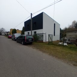 Firma Remontowo-Budowlana Grzegorz Konopka - Nowoczesny dom jednorodzinny z czarno-białą elewacją, widoczny z ulicy, z zaparkowanymi samochodami i elementami ogrodzenia, w pochmurny dzień.
