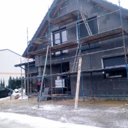 Dom jednorodzinny w trakcie ocieplania elewacji styropianem grafitowym, widoczne rusztowanie, częściowo ośnieżony teren.