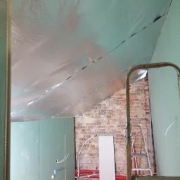 Poddasze w trakcie adaptacji: widoczna izolacja termiczna z folią aluminiową na skośnym suficie, ściany obłożone płytami gipsowo-kartonowymi, fragment odsłoniętej ceglanej ściany, instalacje...