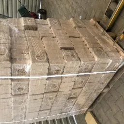 Ułożone na palecie i owinięte folią kostki brykietu drzewnego, widoczne fragmenty wózka widłowego.