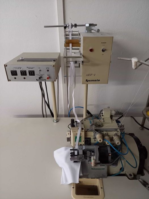 Maszyna szwalnicza Yamato AEF-1 z podajnikiem taśmy elastycznej, widoczny fragment białej tkaniny pod stopką.