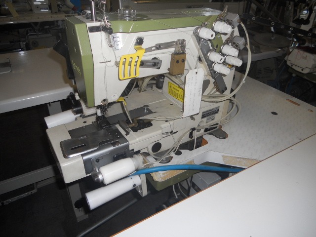 Profesjonalna, przemysłowa maszyna do szycia overlock z wieloma szpulkami nici, widoczne metalowe elementy i białe blaty stołu, oświetlenie studyjne.