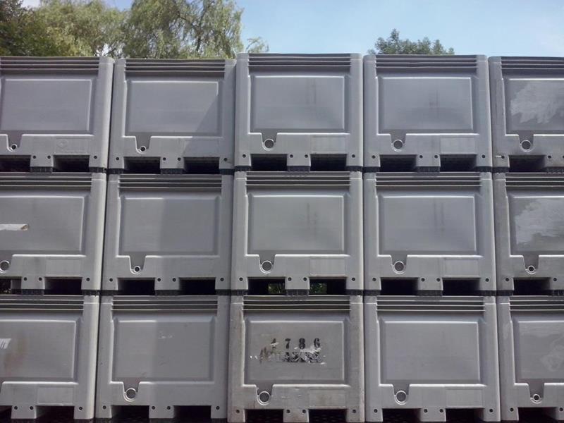 Szare, plastikowe pojemniki wielkogabarytowe ułożone w stos, widoczne elementy konstrukcyjne i mocowania, tło z zielenią drzew.