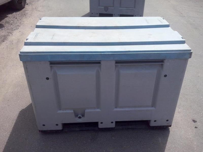 Szary, plastikowy pojemnik z pokrywą na palecie, widoczny otwór drenażowy. W tle fragment drugiego pojemnika i opona samochodu.