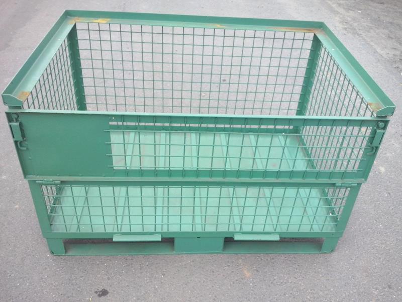 Zielony, metalowy pojemnik siatkowy na palecie, przeznaczony do składowania lub transportu towarów. Widoczne spawy i mocowania.