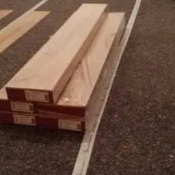 Paczki paneli podłogowych w folii leżące na podłodze, obok ułożone fragmenty paneli, widoczna taśma miernicza.