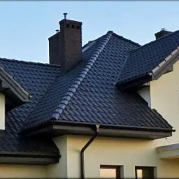 Dom z ciemną dachówką karpiówką, brązowymi oknami PCV i rynnami w kolorze grafitowym, widok z dołu na elewację