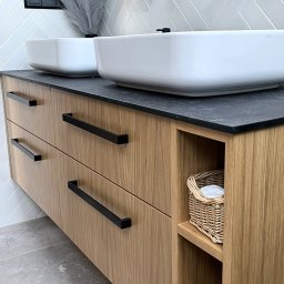 Promeb - Nowoczesna szafka łazienkowa z drewna w Sułkowicach, z czarnym blatem i dwoma białymi umywalkami nablatowymi, czarne minimalistyczne uchwyty, białe płytki ułożone w jodełkę na ścianie.