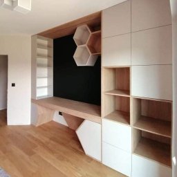 Promeb - Biało-drewniana zabudowa ściany z biurkiem, półkami i szafkami o geometrycznych kształtach, z heksagonalnymi półkami na czarnym tle.