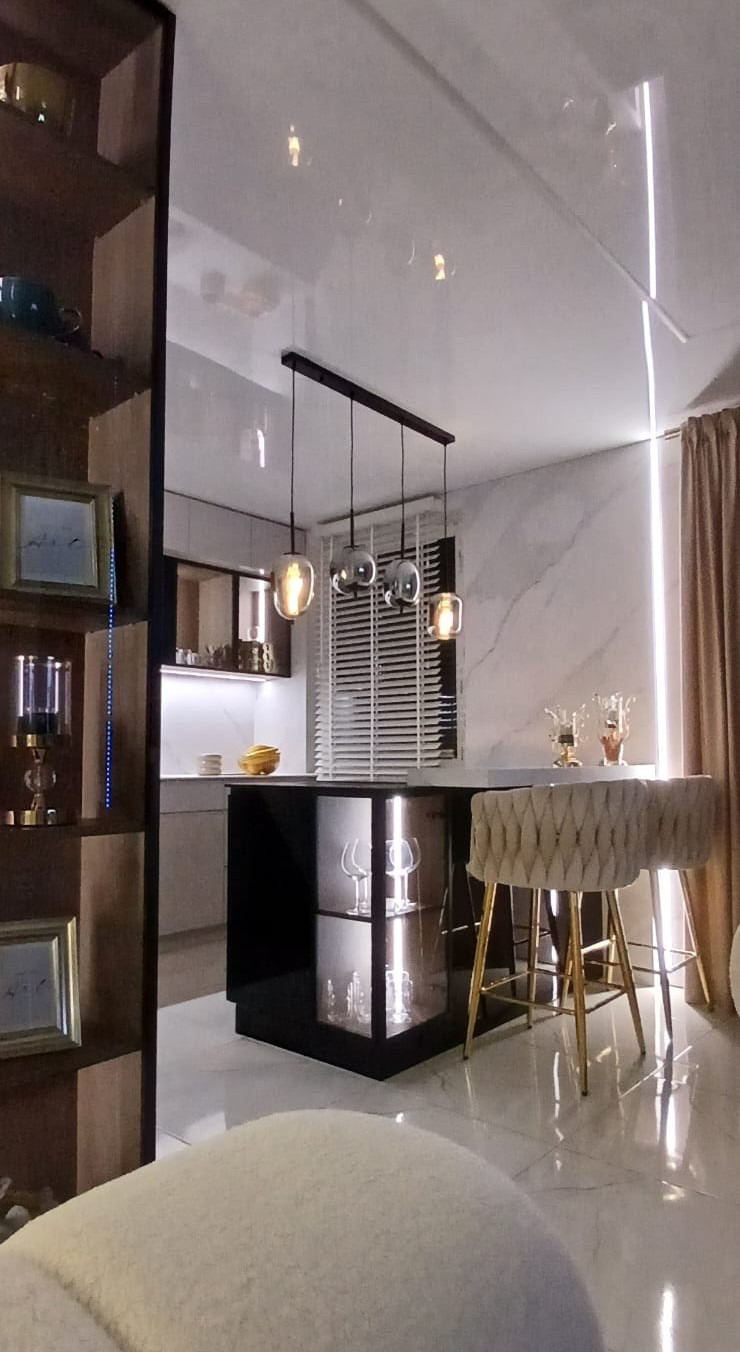 Nowoczesna kuchnia z wyspą, oświetleniem punktowym i marmurową ścianą. Krzesła barowe z welurowym obiciem i złotymi nogami. Elementy szklane i drewniane.