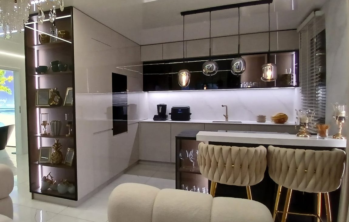 Nowoczesna kuchnia z białymi, lakierowanymi frontami, czarnymi akcentami i oświetleniem LED. Wyspa kuchenna z krzesłami barowymi. Dekoracyjna półka z oświetleniem.