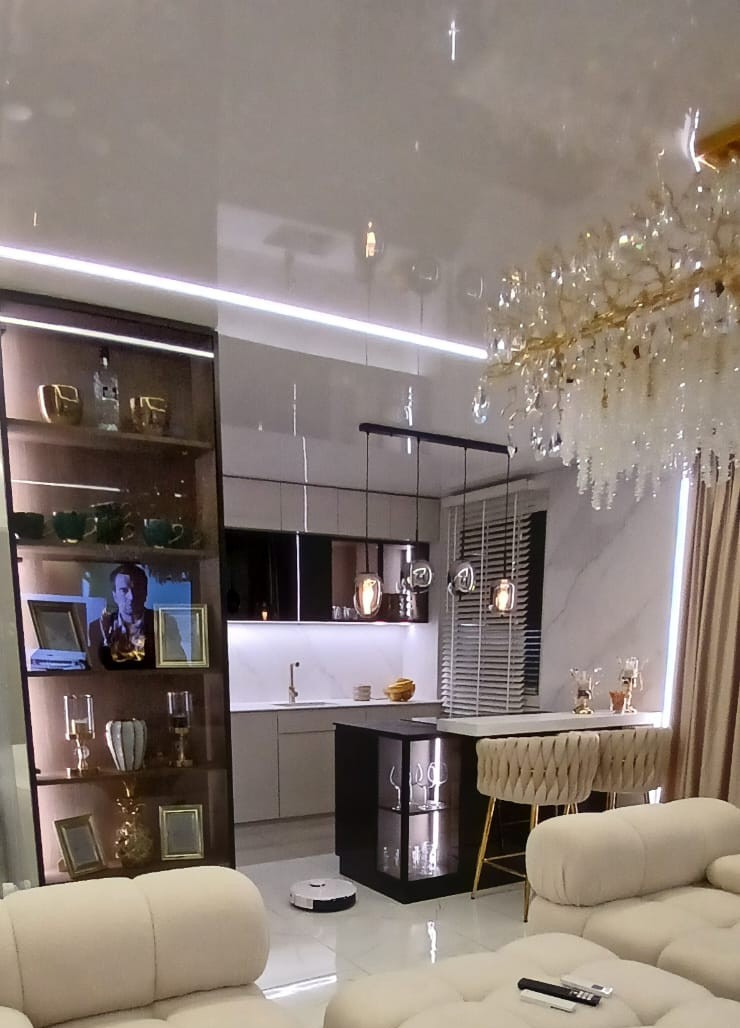 Elegancka kuchnia z wyspą i oświetleniem LED, widok z salonu. Robot sprzątający na podłodze. Kryształowy żyrandol dodaje luksusu. Nowoczesny design.