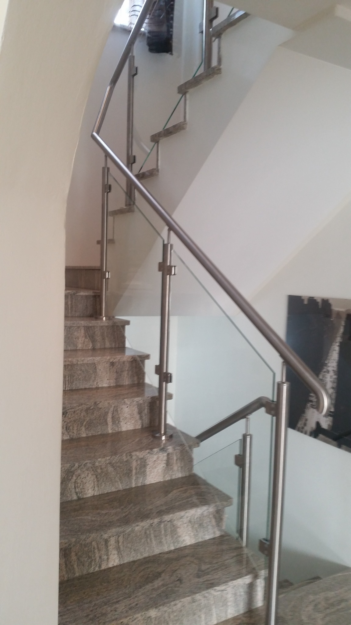 Wewnętrzne schody z kamienia naturalnego z nowoczesną szklaną balustradą i metalowymi poręczami ze stali nierdzewnej, widok z dołu.