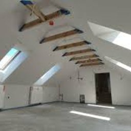 Kur-Rem - Białe poddasze ze skosami i oknami dachowymi. Widoczne drewniane elementy konstrukcyjne i świeżo wylana posadzka. Minimalistyczne wykończenie, surowy stan.