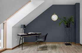 Pokój na poddaszu z biurkiem, krzesłem i rośliną. Ściana pomalowana na ciemny kolor, jasna podłoga, okno w skosie dachu. Zegar w stylu retro na ścianie.