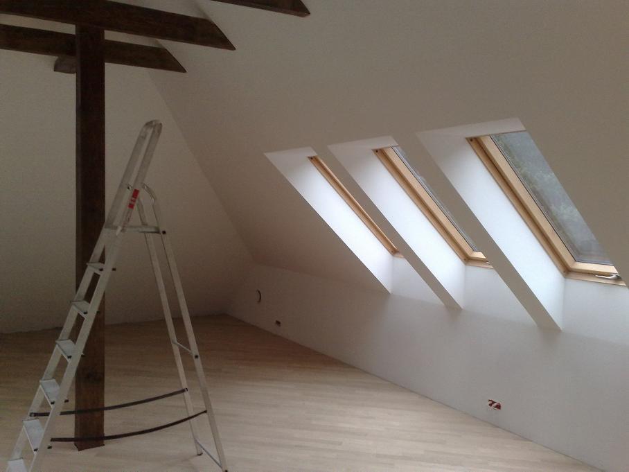 Poddasze po remoncie: trzy okna dachowe w skosie, drewniana belka konstrukcyjna i drabina malarska. Świeżo pomalowane ściany i jasna podłoga.