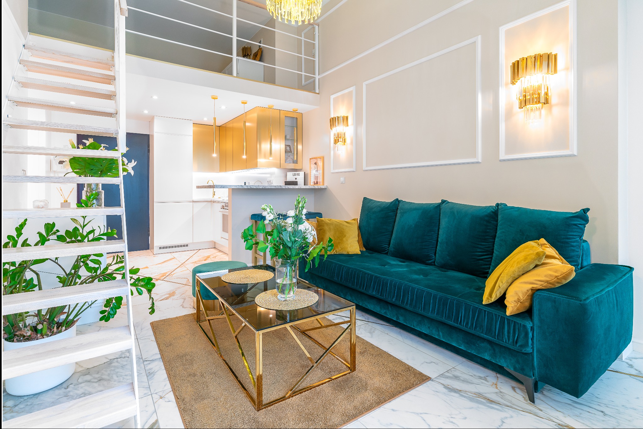 Nowoczesne wnętrze: turkusowa sofa z żółtymi poduszkami, złoty stolik kawowy, biała kuchnia z elementami złota, schody z roślinami i antresola.
