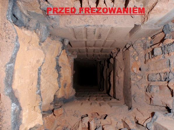 Wnętrze komina przed frezowaniem, widoczne osady i nierówności cegieł. Ujęcie z dołu komina, ciemne wnętrze, ceglana struktura.