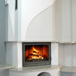 Biały kominek narożny z płomieniami, obudowany kamieniem. Widoczne detale wykończenia i palenisko z palącym się drewnem. Element wystroju wnętrza.