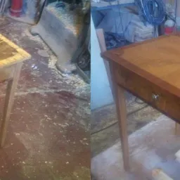 Porównanie stolika drewnianego przed i po renowacji: po lewej stan surowy z uszkodzeniami, po prawej odnowiony z intarsjami i wykończeniem na wysoki połysk, na tle warsztatu stolarskiego.