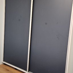 Firma WKTM - Szafa wnękowa z przesuwnymi drzwiami w kolorze grafitowym, białe obramowanie, widoczna podłoga z paneli imitujących drewno.