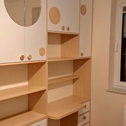 Firma WKTM - Biało-drewniana zabudowa meblowa z okrągłym lustrem i biurkiem, widoczna w pokoju z drewnianą podłogą, oświetlona żarówką.