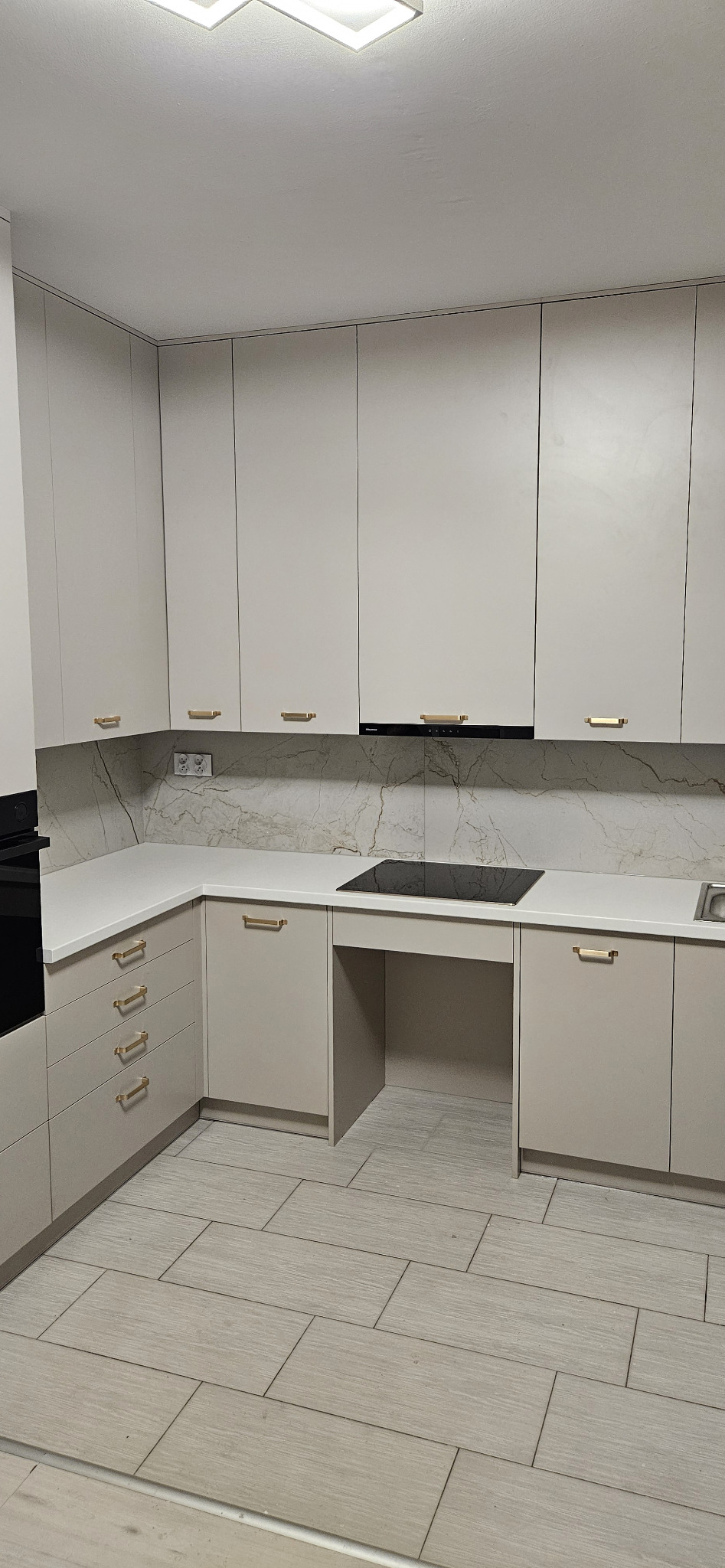 Jasna, nowoczesna kuchnia z beżowymi szafkami, złotymi uchwytami, marmurowym backsplashiem i płytą indukcyjną wkomponowaną w blat.